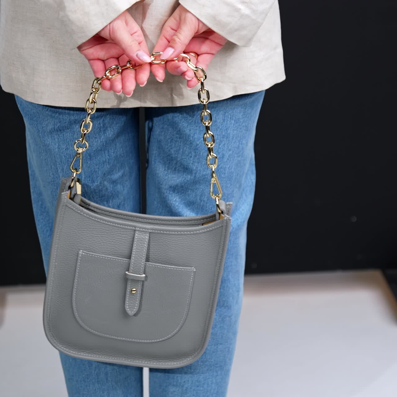 Elegante borsa in pelle grigia con manico a catena dorata tra le mani di una donna. Donna in giacca e jeans che tiene in mano una borsa moderna