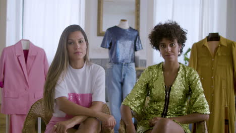 dos hermosas mujeres jóvenes sentadas en un estudio de moda, mirando la cámara