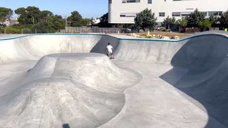 Skater-Macht-Tricks-Im-Beton-Skatepark-Im-Freien-Mit-Wunderschönem-Grünen-Parkhintergrund,-Zeitlupe