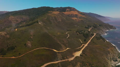 Motorways and footpaths on the sloping mountain. California rocky shore on sunny daytime from aerial view.