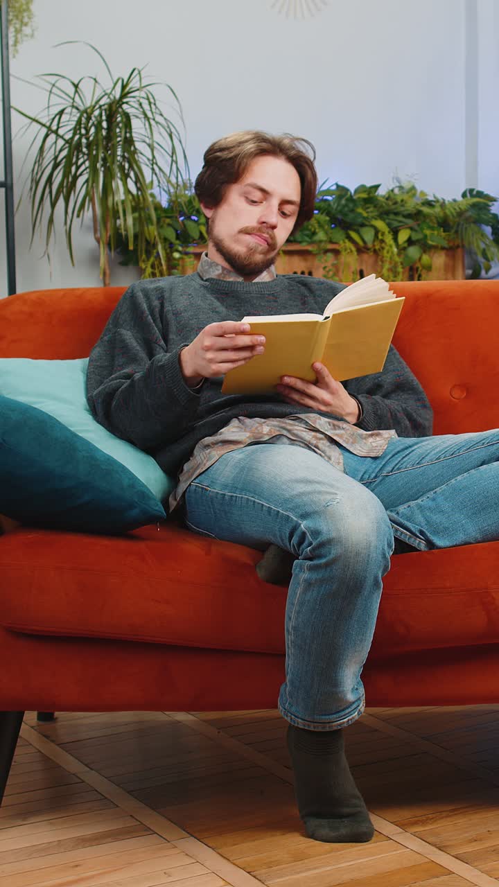 Bearded man reading interesting book turning pages smiling enjoying literature taking a rest at home