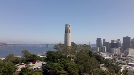 Un-Sereno-Dron-Recorre-Tranquilamente-La-Torre-Coit-En-San-Francisco,-Con-Los-Rascacielos-Del-Centro-Como-Telón-De-Fondo-Sorprendente.