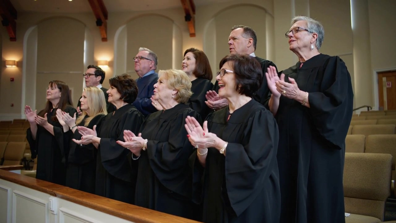 Singing choir on conductor cue, clapping and smiling in church behind wooden rail in black robes