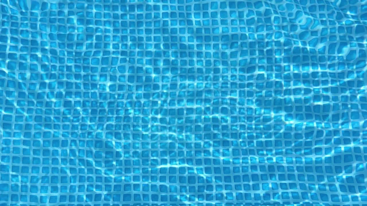 Light reflecting and refracting on the rippling surface of a swimming pool creates a mesmerizing pattern on the blue tiles below, perfect for summer-themed projects