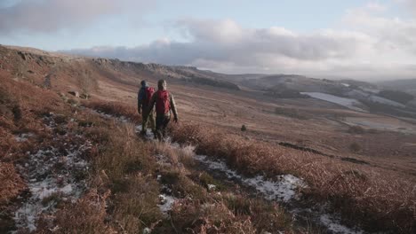 two men hiking along a frozen path through vast, open, countryside moorland in winter as the sun sets