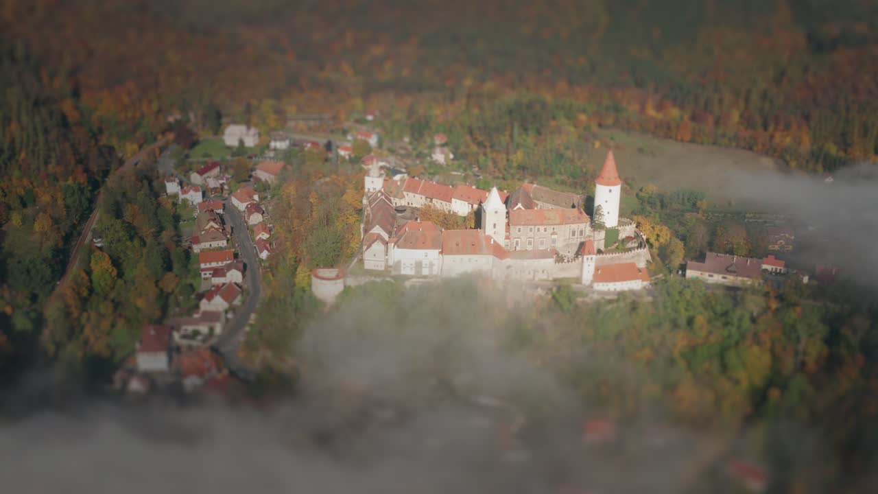 Středověký hrad Křivoklát se tyčí na kopci obklopeném lesy, s vesnicí na jeho úpatí