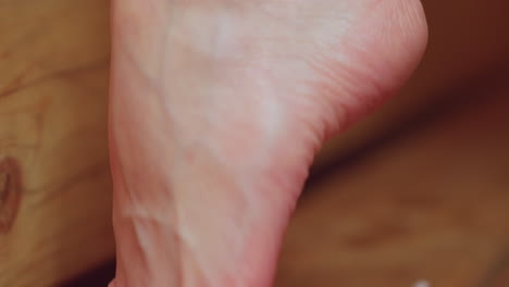 close up of woman applying pink scrub on left leg as droplets fall onto wooden sauna bench under steam ambient warmth in relaxing spa exfoliation ritual with towel wrapped waist and serene vibe