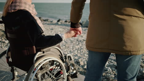 couple holding hands on the beach with a wheelchair