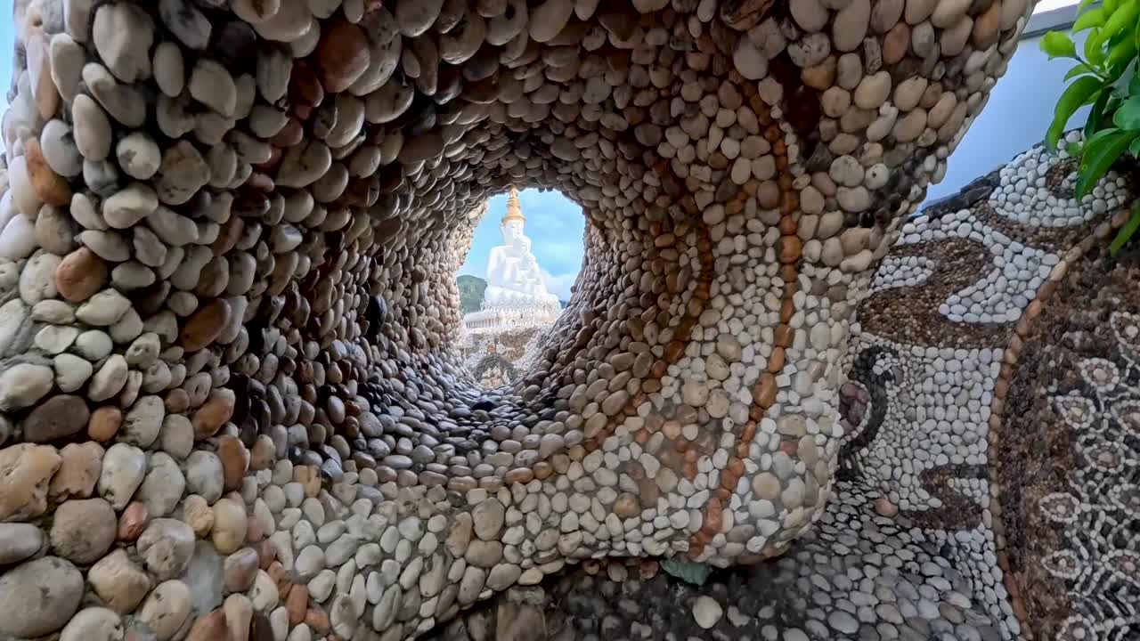 Sculture decorative in mosaico di pietra e passerelle piastrellate colorate al tempio Wat Pha Sorn Kaew con archi dorati e una statua del Buddha bianca sullo sfondo