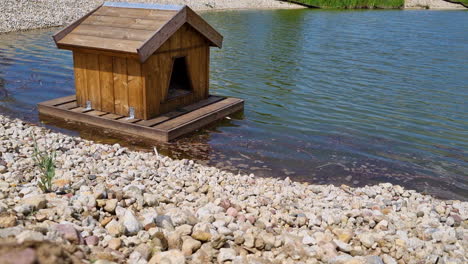 a small wooden duck house floats on the surface of the lake