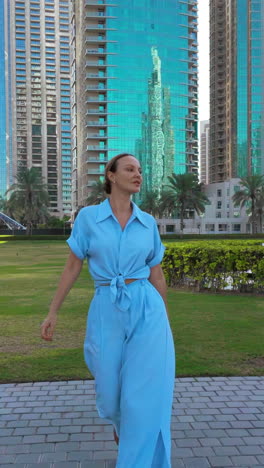 woman in a light blue outfit walks in a park near skyscrapers