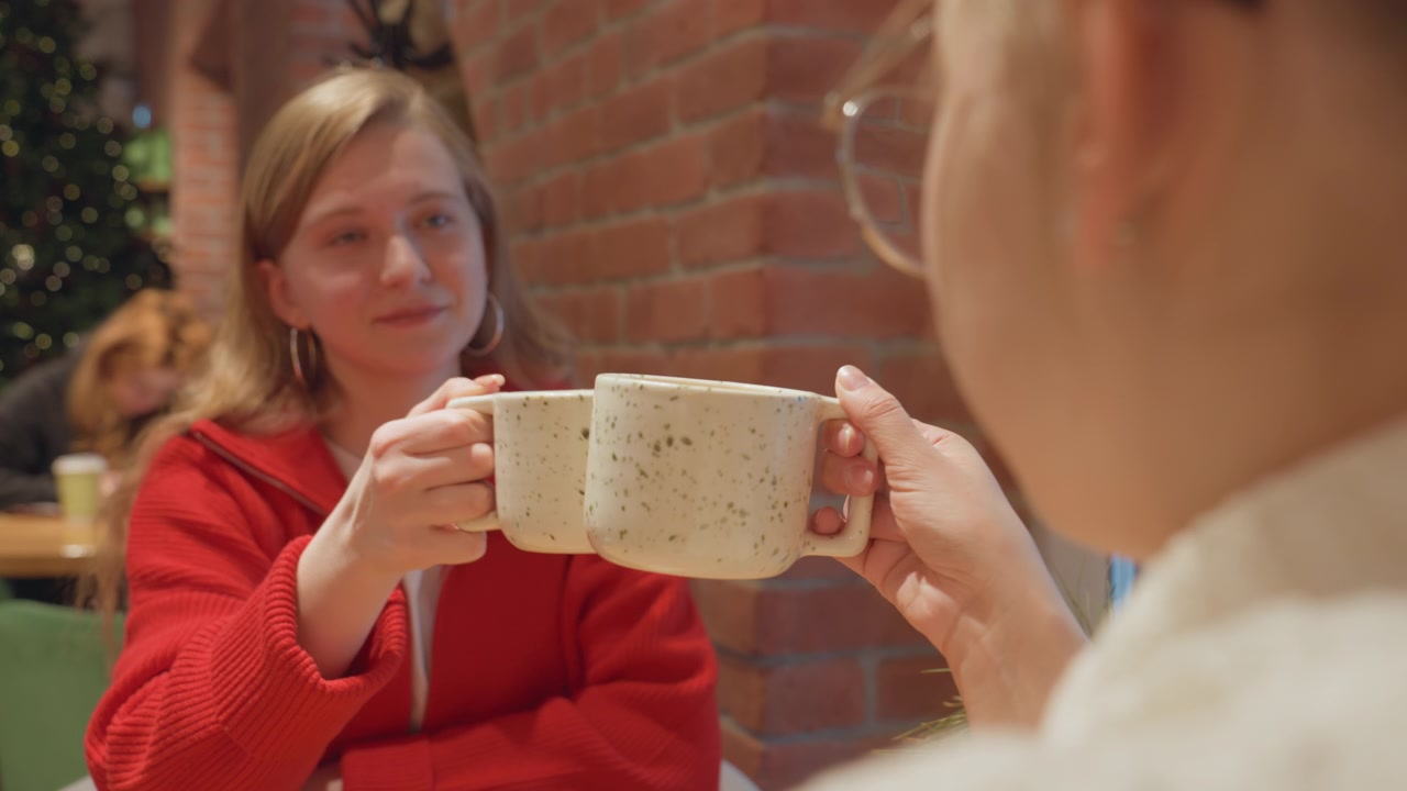 Due giovani donne che brindano con le tazze in un caffè accogliente