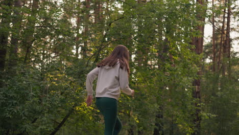 young lady sprints in forest in evening. woman runs intensity moving arms for active cardio workout. female athlete does sports running past trees