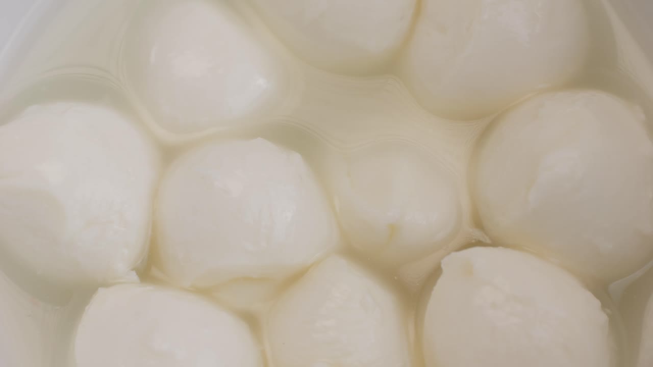 Mozzarella cheese in bowl close-up. Mozzarella is a semi-soft non-aged cheese prepared by the pasta filata method From Italian cow's milk. Mozzarella is used for most types of pizza and several pasta dishes or served with sliced tomatoes and basil in Caprese salad.