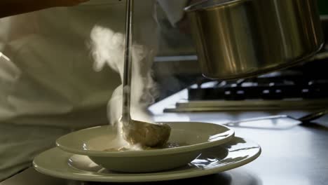 female chef pouring soup with ladle into a plate in kitchen 4k