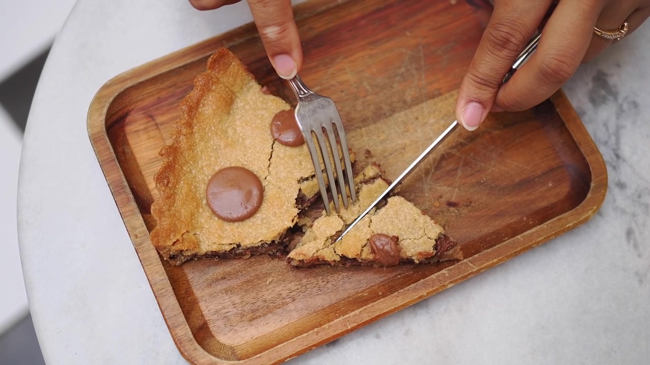 Person skærer et stykke chokoladechip cookie-tærte