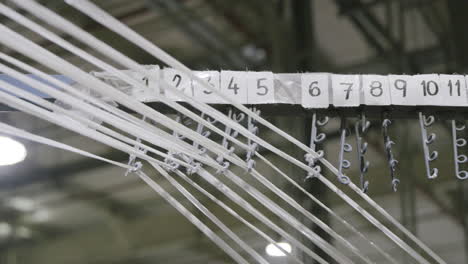 slow motion footage of a group of white ribbons beings threaded through circle loops with numbers above in a factory