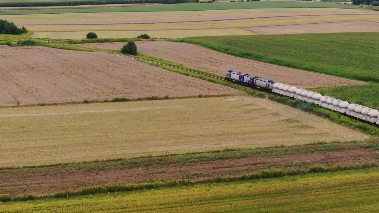 Modern freight train with industrial cargo moves through rural Poland, aerial view
