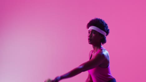 Video-of-focused-african-american-female-tennis-player-hitting-ball-on-neon-pink-lightning