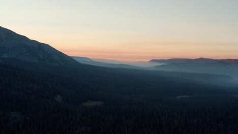 beautiful right trucking aerial drone shot of the stunning wild uinta wasatch cache national forest in utah with large pine trees below and stunning mountains covered in mist during a summer sunrise