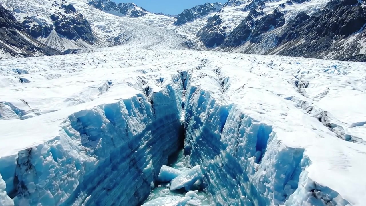 Paesaggio glaciale mozzafiato: viste mozzafiato di fessure e crepacci su un maestoso ghiacciaio circondato da imponenti cime montuose sotto cieli azzurri e limpidi.
