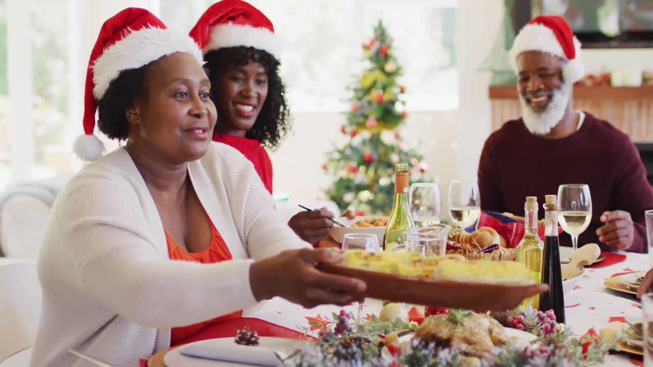 mujer mayor afroamericana en el sombrero de santa pasando el plato de comida de su hijo y nieto mientras estaba sentada