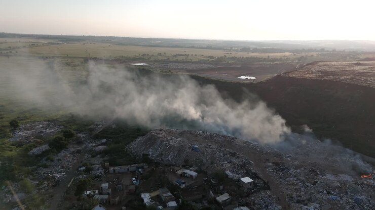 A static drone shot captures the coexistence of a rural township village and a waste processing plant in South Africa