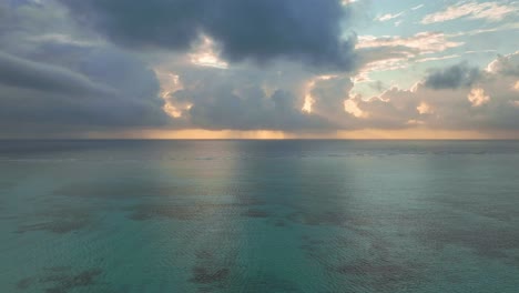 Drone-captures-the-setting-sun-over-Paje,-Zanzibar,-painting-the-sky-with-swirling-clouds-and-flying-over-the-turquoise-ocean-and-coral-reef