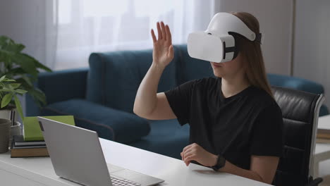 woman is using vr head-mounted display connected to laptop viewing display and screen gesticulating by hands for control medium female portrait at home