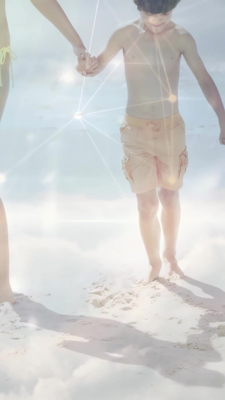 縦型動画：両親の手を握り、きらめく太陽の光が降り注ぐビーチを歩く男の子、旅行広告。