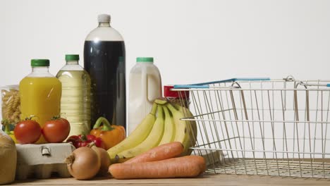 studio shot of basic food items next to supermarket wire shopping basket 1