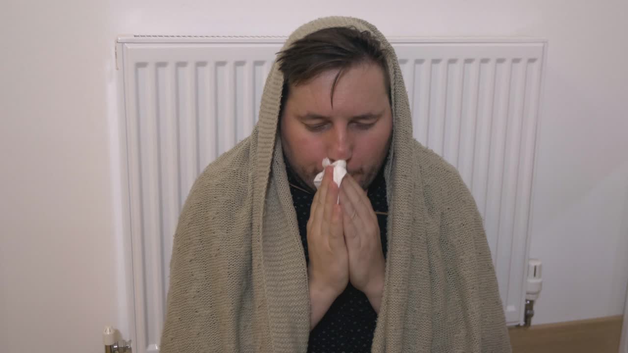 hombre caucásico cubierto con una manta soplando la nariz corriendo tiene fiebre estornudo frío en el tejido sentado solo en la habitación, síntomas alérgicos enfermos tosiendo en casa, concepto de gripe