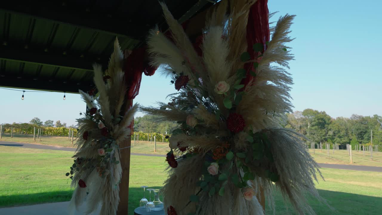 A wide shot of a boho-style wedding arch decorated with pampas grass and florals, framed by a serene vineyard backdrop under soft afternoon light in South Georgia.