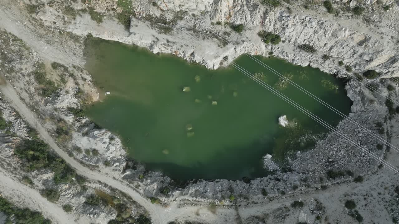 Green water gradually filling quarry basin during descending camera movement, revealing submerged rocks and dense algae beneath water surface