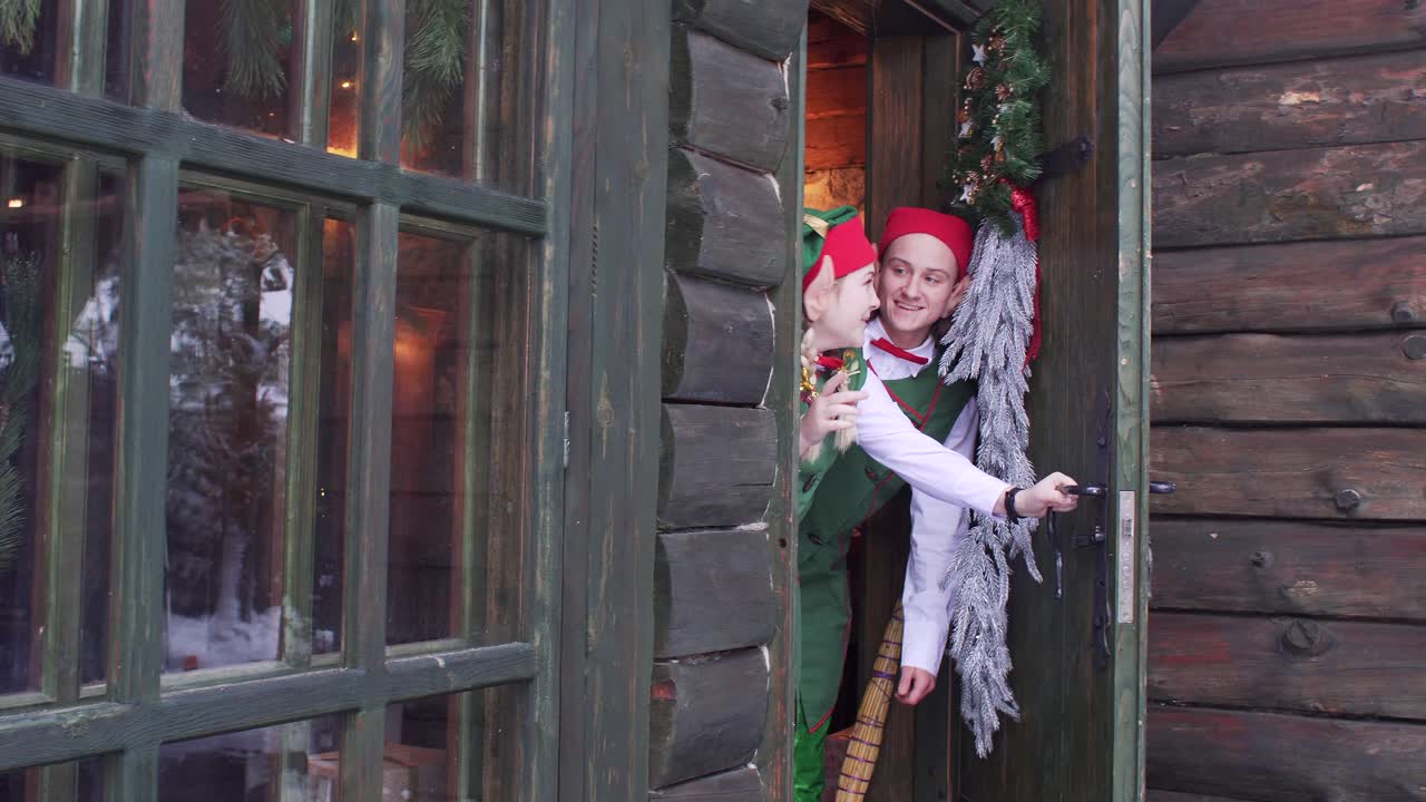 Elves peep out from behind a wooden door of santa claus residence