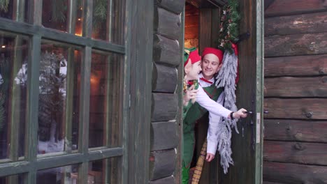 elves peep out from behind a wooden door of santa claus residence