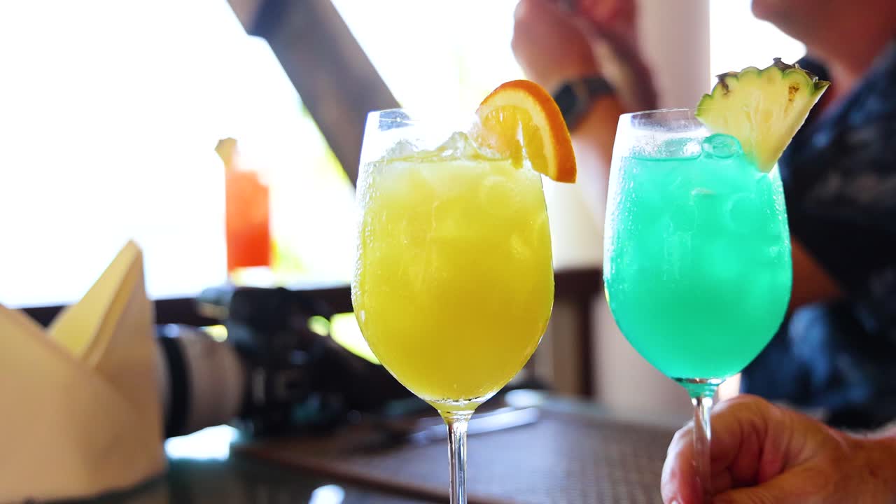 Vibrant yellow and blue cocktails with fruit garnishes on a table, captured in bright natural lighting