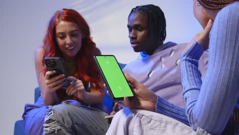 close up of woman with green screen mobile phone sitting with gen z friends talking and sharing posts 2