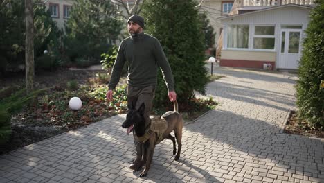 a man walks by house yard with service dog in military protective collar