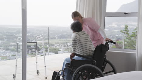 smiling caucasian nurse with senior african american woman patient in wheelchair, slow motion