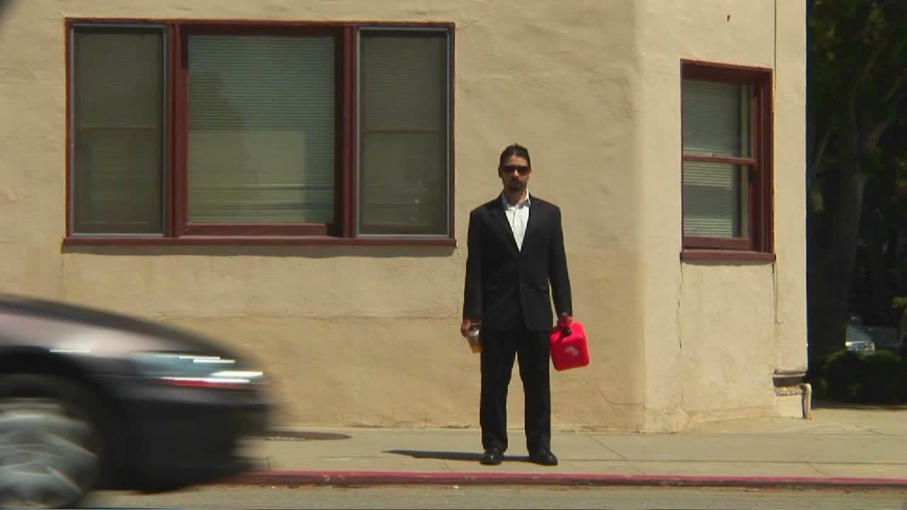 가스통을 들고 있는 남자가 교통량이 많은 보도에 서 있다