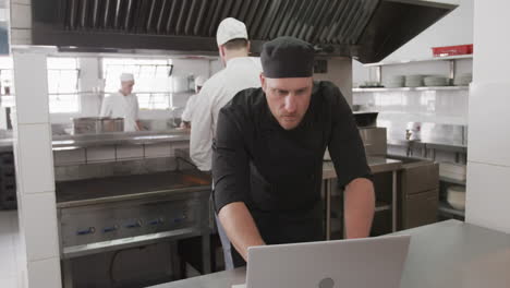 caucasian male chef using laptop in kitchen, slow motion