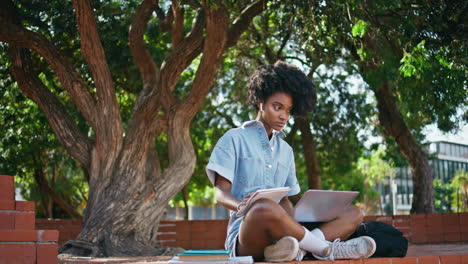 niña tomando un curso en línea en una computadora portátil tomando notas en el cuaderno sentada bajo los árboles