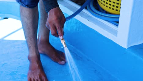 a person washes a blue boat deck with a hose, under bright daylight, in phuket
