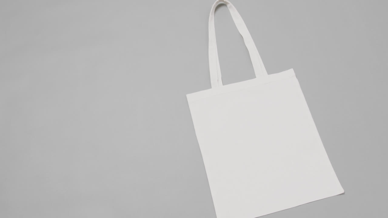 Primo piano di borsa bianca su sfondo grigio, con spazio per il testo, in slow motion