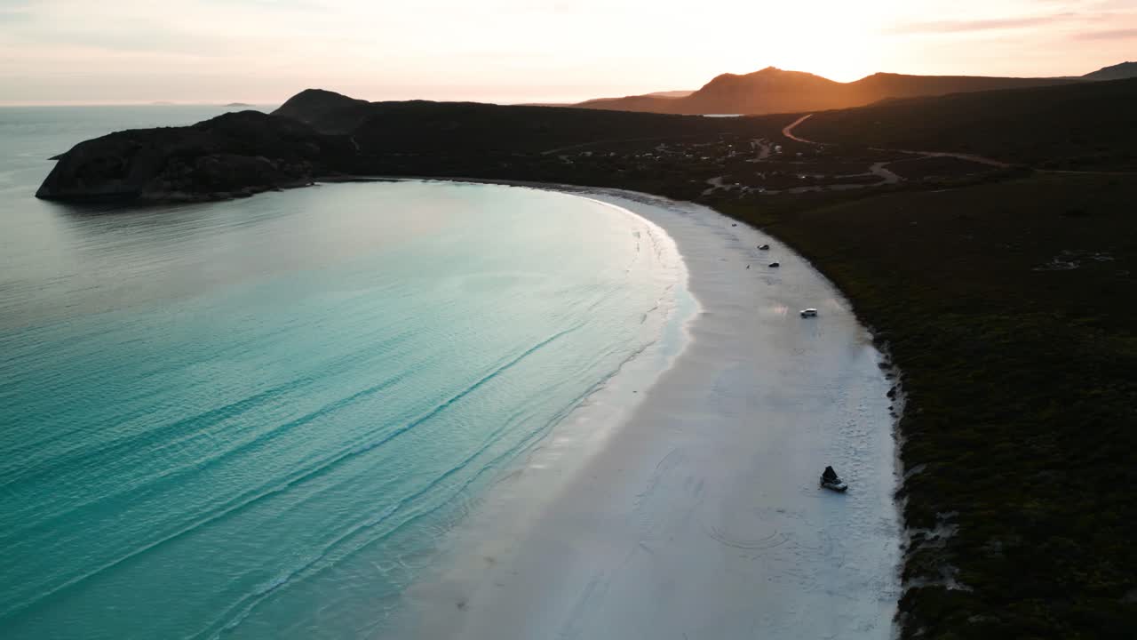 drone disparado sobre lucky bay en el parque nacional de cape legrand al atardecer con 4wd en la playa y el sol en el fondo, australia occidental