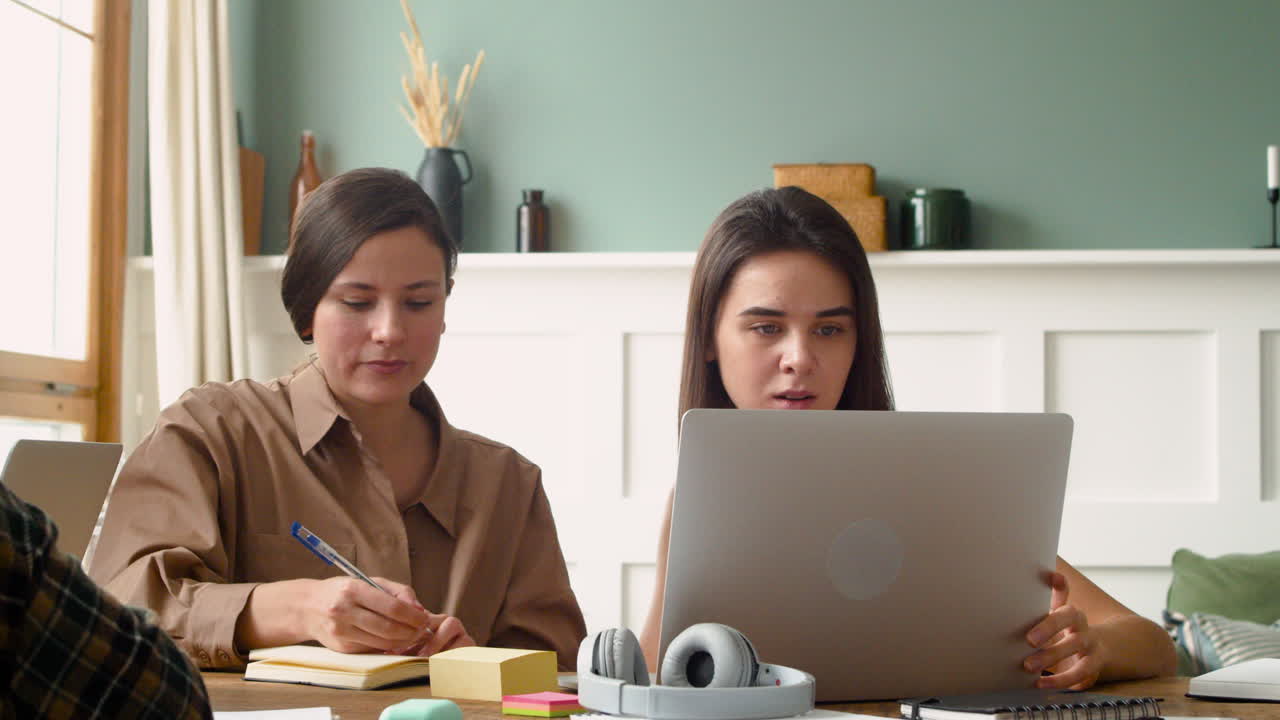 la cámara se enfoca en dos chicas de un grupo de estudio que están escribiendo y mirando una laptop