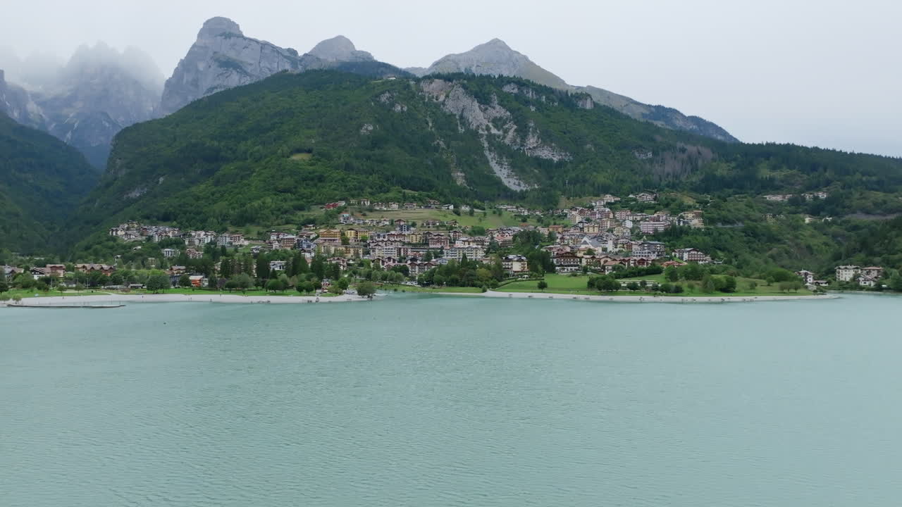Aerial footage flying away from the town of Molveno revealing more of the lake and the mountains in the background.