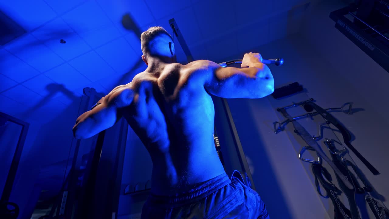 Brutal strong athletic men pumping up muscles. Doing workout on sport equipment - muscular bodybuilder doing exercises in gym with naked torso. Fitness and bodybuilding concept. Video from the back.