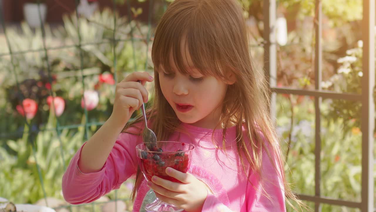 linda niña de 6 o 7 años comiendo gelatina de postre de frutas en el jardín de verano video en cámara lenta